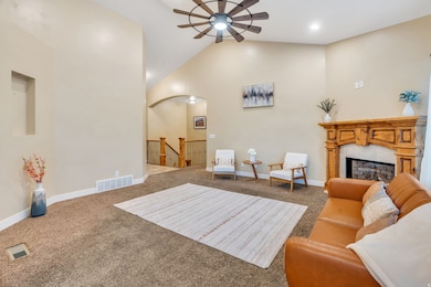 Carpeted living room featuring high vaulted ceiling, arched walkways, a fireplace, and a ceiling fan