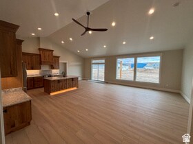 Kitchen with open floor plan, an island with sink, light wood finished floors, a ceiling fan, and high vaulted ceiling