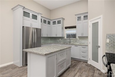 Kitchen with freestanding refrigerator, light stone counters, dark wood-style flooring, and decorative backsplash