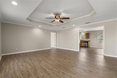 Unfurnished living room with a tray ceiling, ceiling fan, wood finished floors, crown molding, and recessed lighting