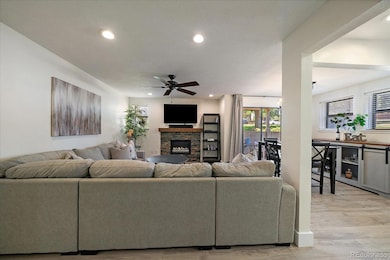 Bright living room with recessed lighting, ceiling fan, and electric fireplace with wood mantle.