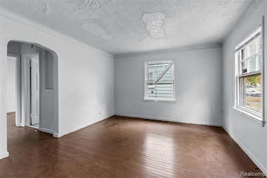 Spare room with arched walkways, dark wood-style flooring, and a textured ceiling