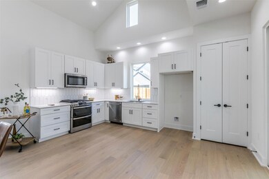 Kitchen featuring stainless steel appliances, white cabinetry, high vaulted ceiling, recessed lighting, and light wood-style floors