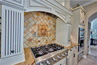 Kitchen with arched walkways, light stone counters, custom range hood, stainless steel appliances, and decorative backsplash