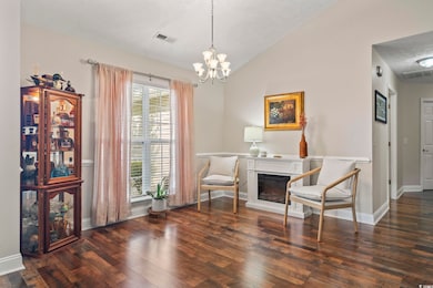 Living area with wood finished floors, a chandelier, a glass covered fireplace, and lofted ceiling