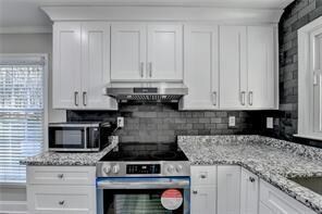 Kitchen with appliances with stainless steel finishes, under cabinet range hood, white cabinets, and backsplash