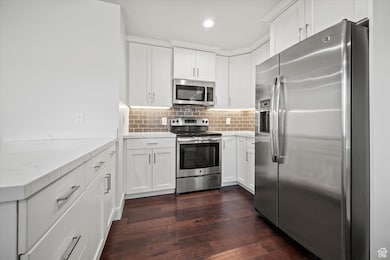 Kitchen featuring appliances with stainless steel finishes, dark wood finished floors, tasteful backsplash, white cabinetry, and light stone counters