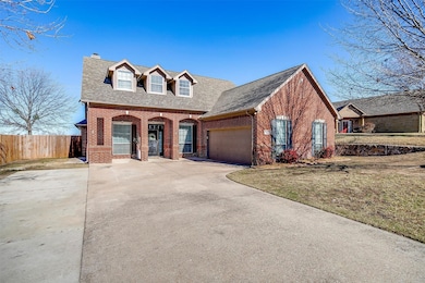 View of front facade with brick siding, driveway, a shingled roof, a porch, and a chimney