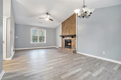 Unfurnished living room with lofted ceiling, wood finished floors, a ceiling fan, a stone fireplace, and a chandelier