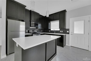 Kitchen featuring decorative light fixtures, light tile flooring, a kitchen island, backsplash, and appliances with stainless steel finishes