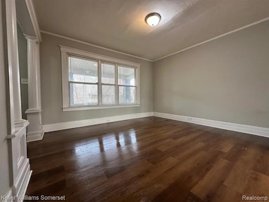 Spare room featuring decorative columns, dark wood-type flooring, ornamental molding, and a textured ceiling