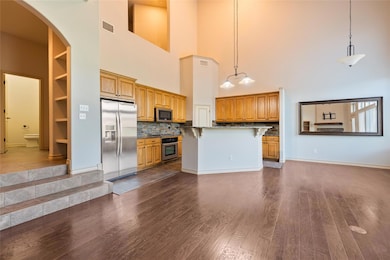 Kitchen featuring stainless steel appliances, decorative backsplash, hanging light fixtures, a breakfast bar, and dark wood-type flooring