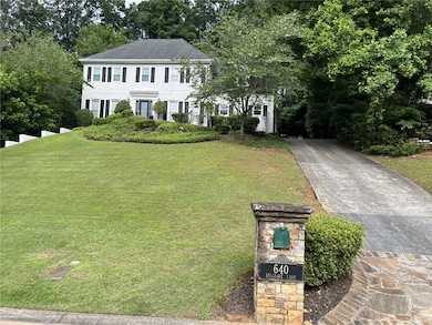 Colonial home with a front lawn, driveway, and view of wooded area
