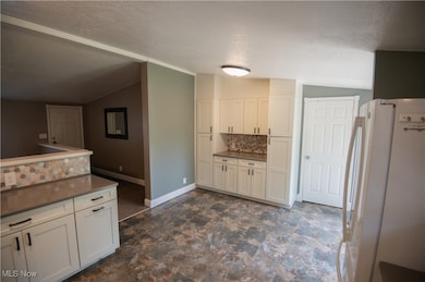 Kitchen featuring backsplash, freestanding refrigerator, lofted ceiling, a textured ceiling, and white cabinetry