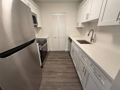 Kitchen with appliances with stainless steel finishes, backsplash, white cabinetry, dark wood-type flooring, and light stone countertops