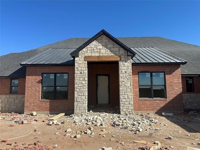 View of front of house with a standing seam roof, a metal roof, stone siding, brick siding, and roof with shingles