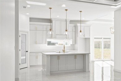 Kitchen with decorative light fixtures, a center island with sink, white cabinetry, and sink