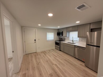 Kitchen featuring appliances with stainless steel finishes, a sink, gray cabinetry, light countertops, and light wood finished floors