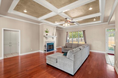 Living room with ornamental molding, wood finished floors, beam ceiling, a tile fireplace, and coffered ceiling