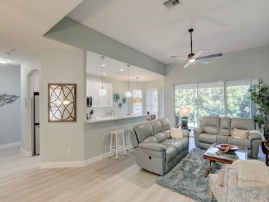 Living area featuring light wood-style flooring, ceiling fan, arched walkways, and recessed lighting