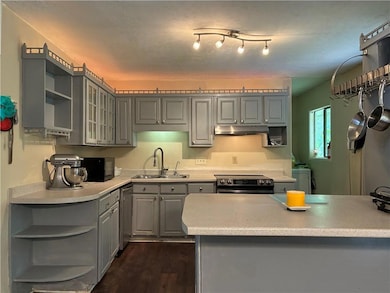 Kitchen with open shelves, gray cabinets, a sink, under cabinet range hood, and range with electric stovetop