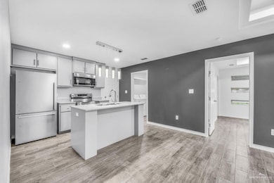 Kitchen with appliances with stainless steel finishes, decorative light fixtures, gray cabinetry, a center island with sink, and washing machine and dryer