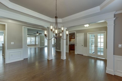Unfurnished dining area featuring a decorative wall, dark wood finished floors, a wainscoted wall, crown molding, and a ceiling fan