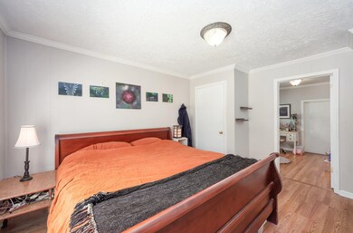 Bedroom with light wood-style floors, crown molding, and a textured ceiling