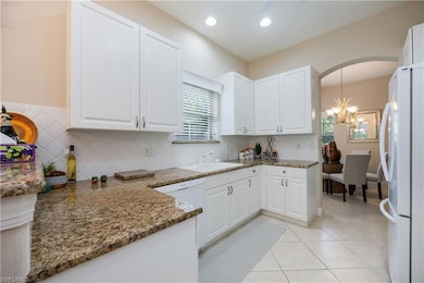 Kitchen with white cabinetry, tasteful backsplash, white appliances, light tile patterned floors, and light stone countertops