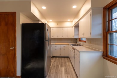 Kitchen with light countertops, freestanding refrigerator, white cabinetry, decorative backsplash, and light wood finished floors