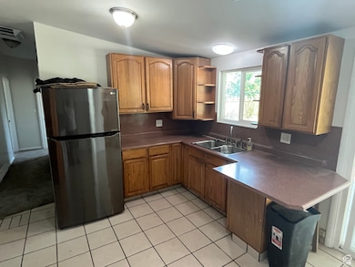 Kitchen featuring freestanding refrigerator, a peninsula, light tile patterned floors, open shelves, and a kitchen bar