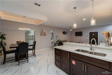 Kitchen with sink, pendant lighting, dark brown cabinets, a tray ceiling, and light tile floors