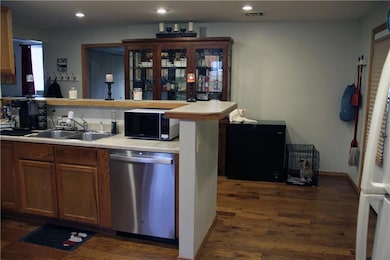 Kitchen with light countertops, dishwasher, dark wood-type flooring, black fridge, and a peninsula
