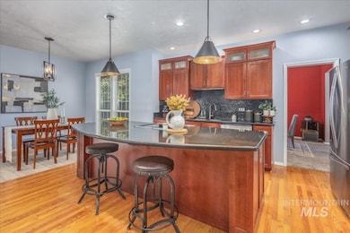 Kitchen featuring stainless steel appliances, dark countertops, light wood-style flooring, backsplash, and a kitchen island