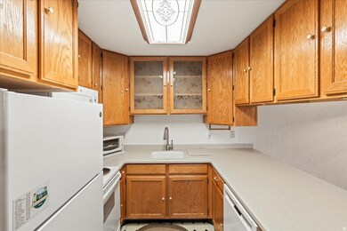 Kitchen with white appliances, brown cabinets, light countertops, and glass insert cabinets