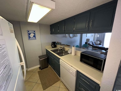 Kitchen featuring light countertops, light tile patterned floors, white appliances, and a textured ceiling