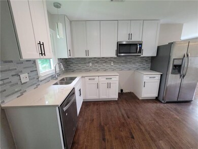 Kitchen with appliances with stainless steel finishes, dark wood-style floors, and white cabinets