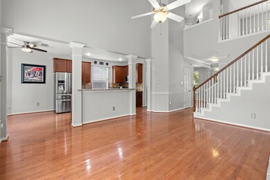 Unfurnished living room with a ceiling fan, light wood-style flooring, decorative columns, and a towering ceiling