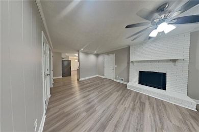 Unfurnished living room with wood finished floors, a ceiling fan, a brick fireplace, crown molding, and recessed lighting