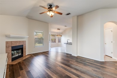 Unfurnished living room with dark wood-style flooring, ceiling fan, vaulted ceiling, a tiled fireplace, and arched walkways