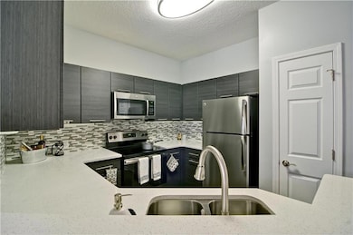 Kitchen featuring tasteful backsplash, light stone counters, appliances with stainless steel finishes, and sink