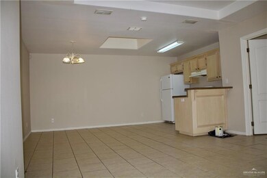 Kitchen featuring freestanding refrigerator, dark countertops, under cabinet range hood, light brown cabinets, and visible vents