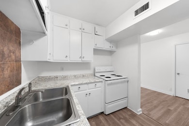Kitchen featuring electric range, white cabinets, light wood-type flooring, and light countertops