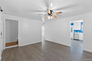 Unfurnished living room with wood finished floors, ceiling fan, and stairway