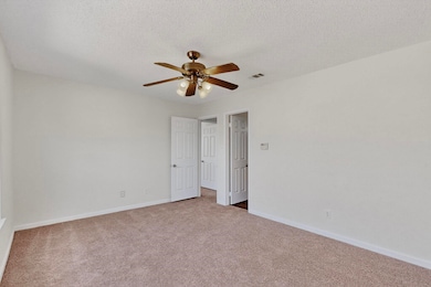 Unfurnished bedroom with light carpet, a ceiling fan, and a textured ceiling