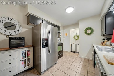 Kitchen featuring stainless steel fridge, light tile patterned floors, black electric range, dishwasher, and light countertops