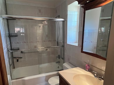 Bathroom featuring vanity, toilet, tile walls, decorative backsplash, and bath / shower combo with glass door