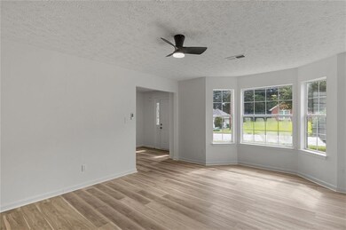 Empty room featuring healthy amount of natural light, light wood-type flooring, ceiling fan, and a textured ceiling