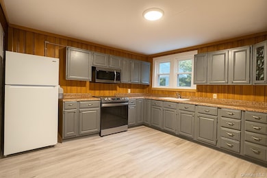 Kitchen featuring wood walls, gray cabinetry, stainless steel appliances, light countertops, and light wood-style flooring