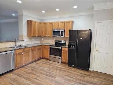 Kitchen featuring appliances with stainless steel finishes, a sink, brown cabinets, dark stone counters, and light wood finished floors